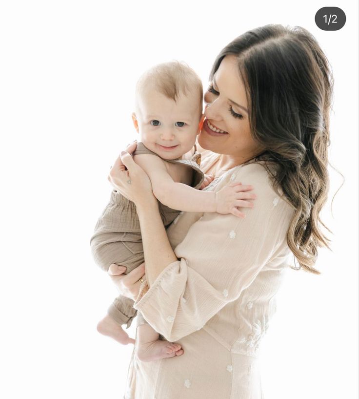 a woman holding a baby in her arms and smiling at the camera with white background