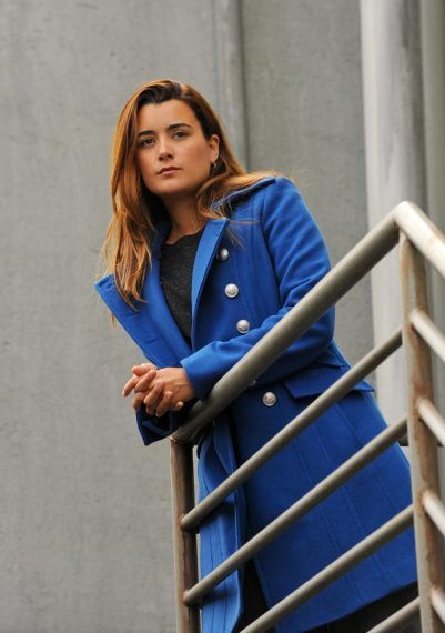 a woman in a blue coat is standing on some stairs and looking off into the distance