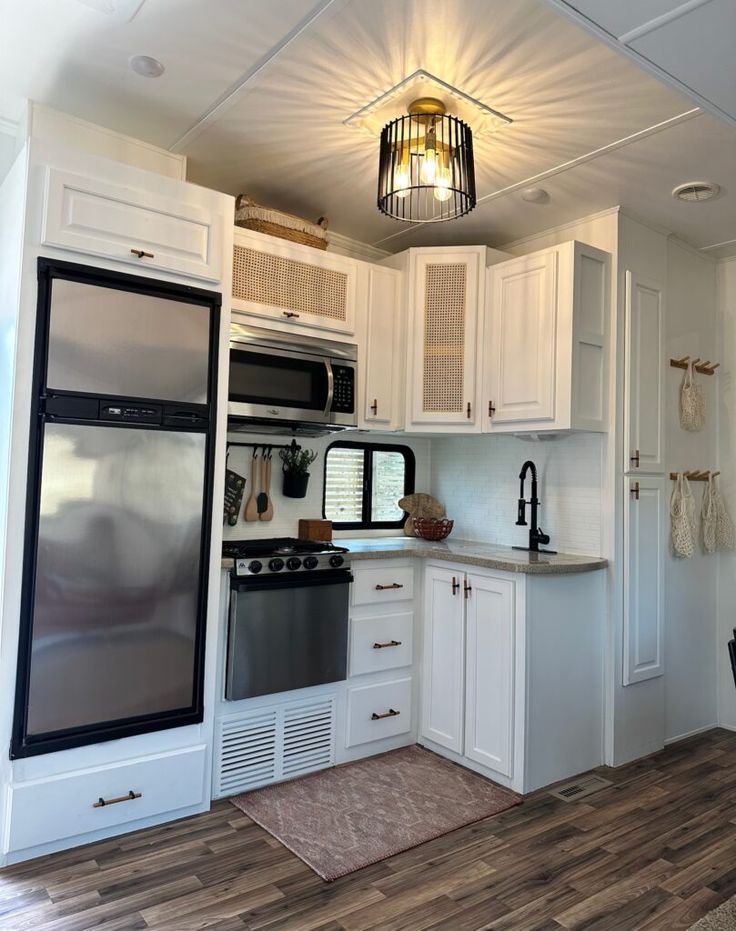 a kitchen with white cabinets and stainless steel appliance, wood flooring and pendant light fixture