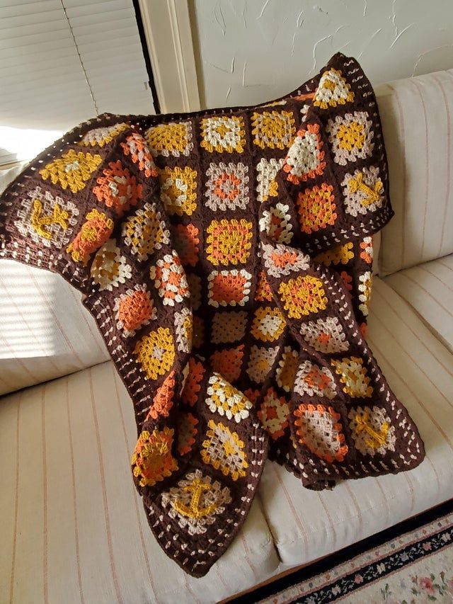 a crocheted blanket sitting on top of a white couch next to a window