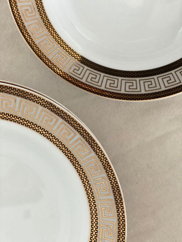 two white and gold plates sitting next to each other