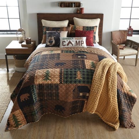 a bed in a room with a brown and black quilt on the comforter next to two chairs