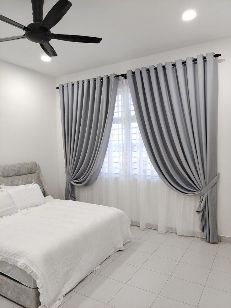 a white bed sitting under a window next to a ceiling fan