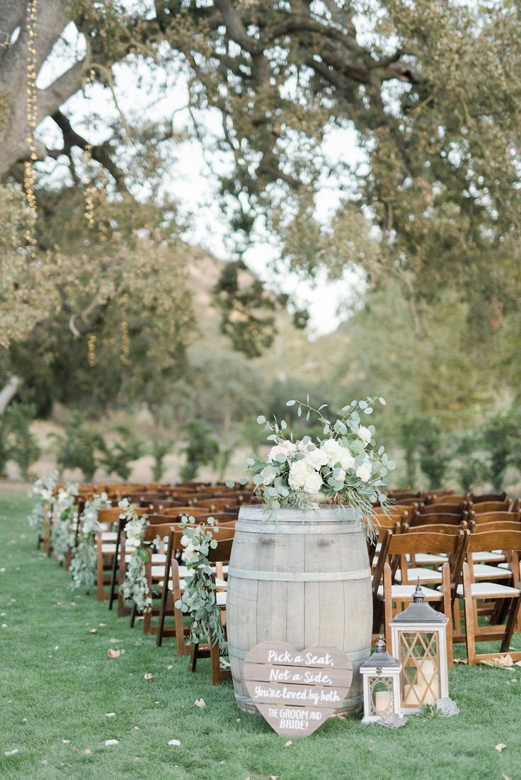 an outdoor ceremony set up with wooden chairs and white flowers on the back of a barrel