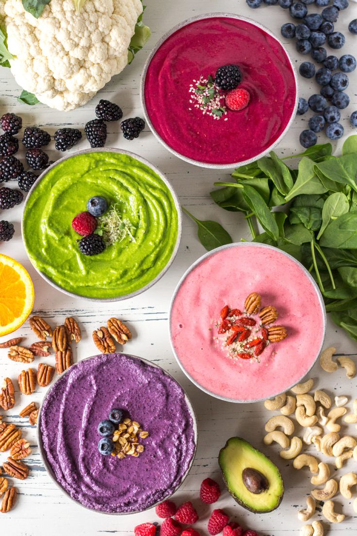 bowls filled with different fruits and vegetables on top of a white table next to nuts