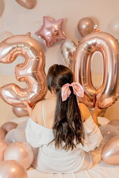 a woman sitting on top of a bed surrounded by balloons and heliums in the shape of numbers