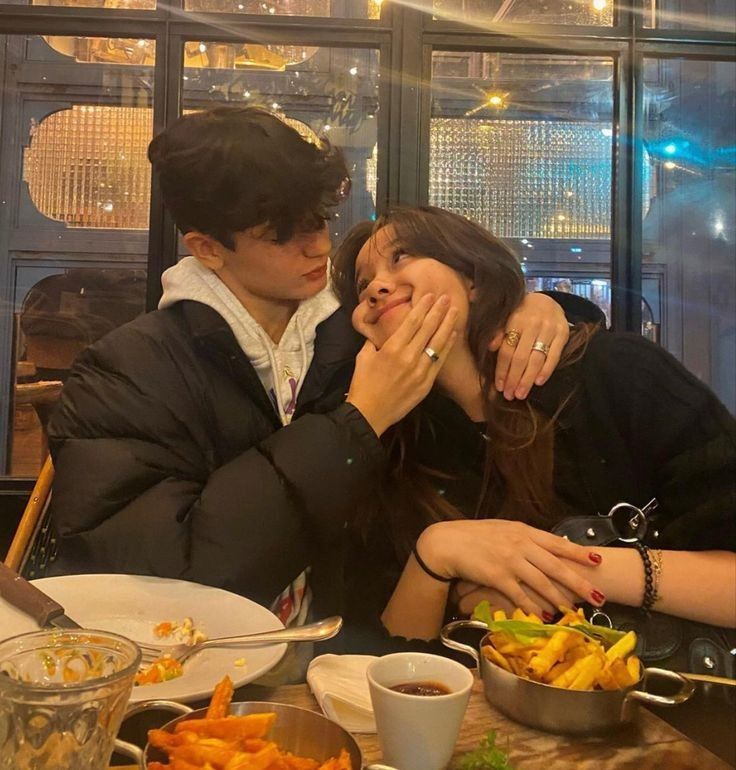 two people sitting at a table with food in front of them and one woman covering her mouth