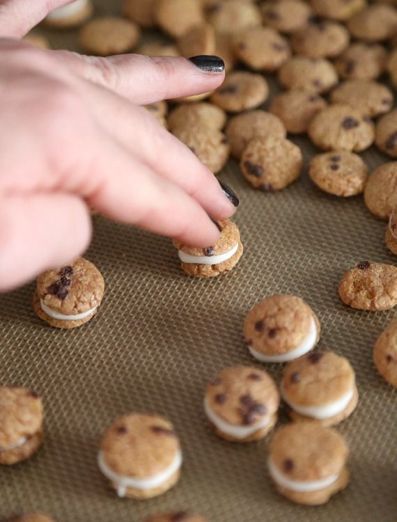 a person reaching for some cookies on a baking sheet with other cookies scattered around them