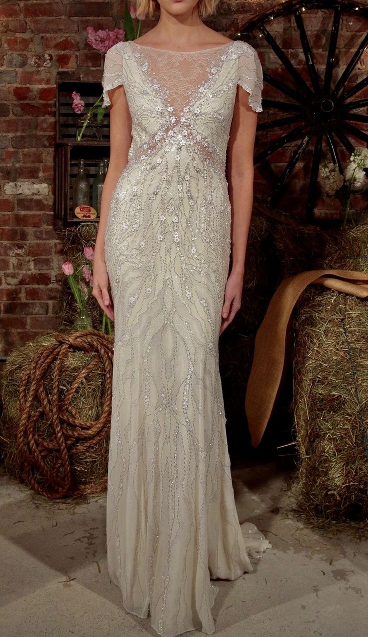 a woman standing in front of a brick wall wearing a dress with beading on it