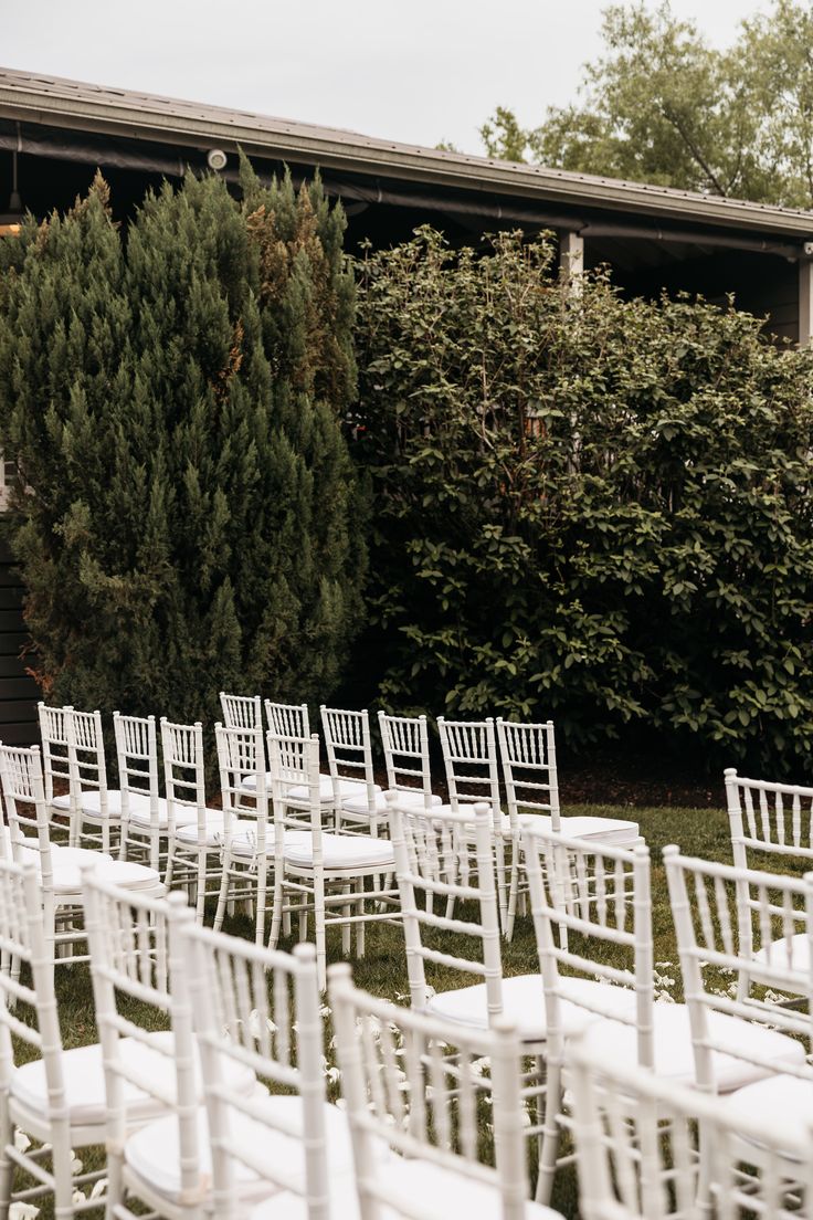 rows of white chairs are lined up in front of a building with trees and bushes