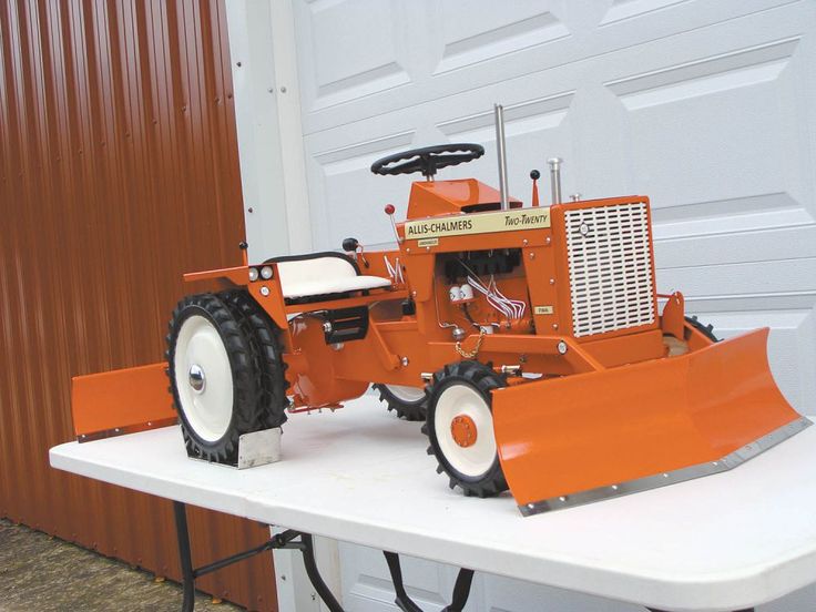 an orange tractor sitting on top of a white table in front of a garage door