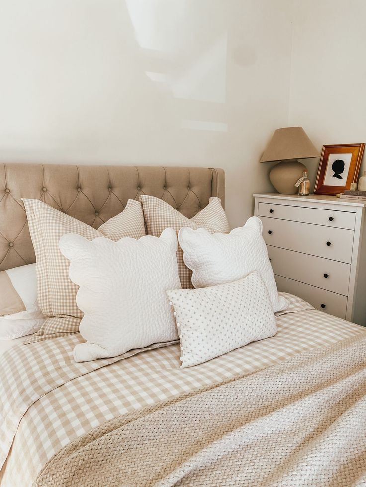 a bed with several pillows on top of it next to a night stand and dresser