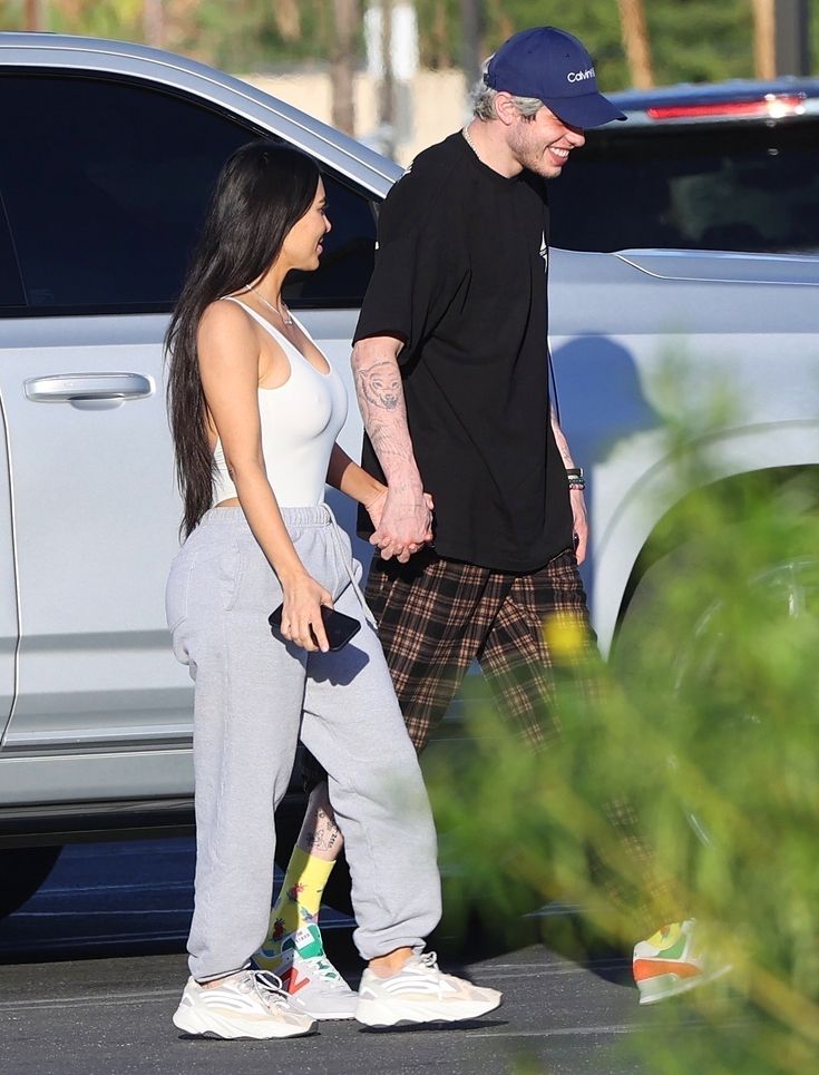 a man and woman are walking together in front of a car while another person is holding hands