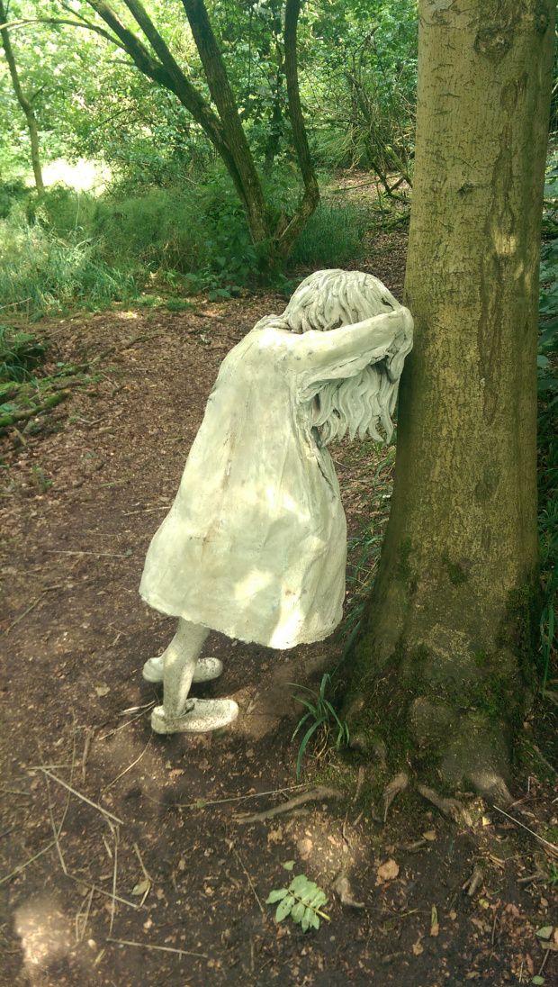 a white statue leaning against a tree in the woods with it's head on its back