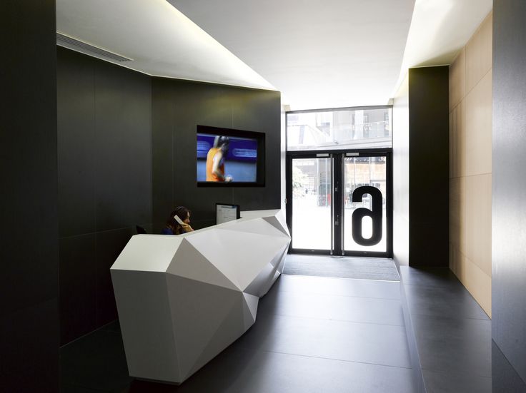 a modern lobby with black walls and white geometric design on the front desk, along with a large television