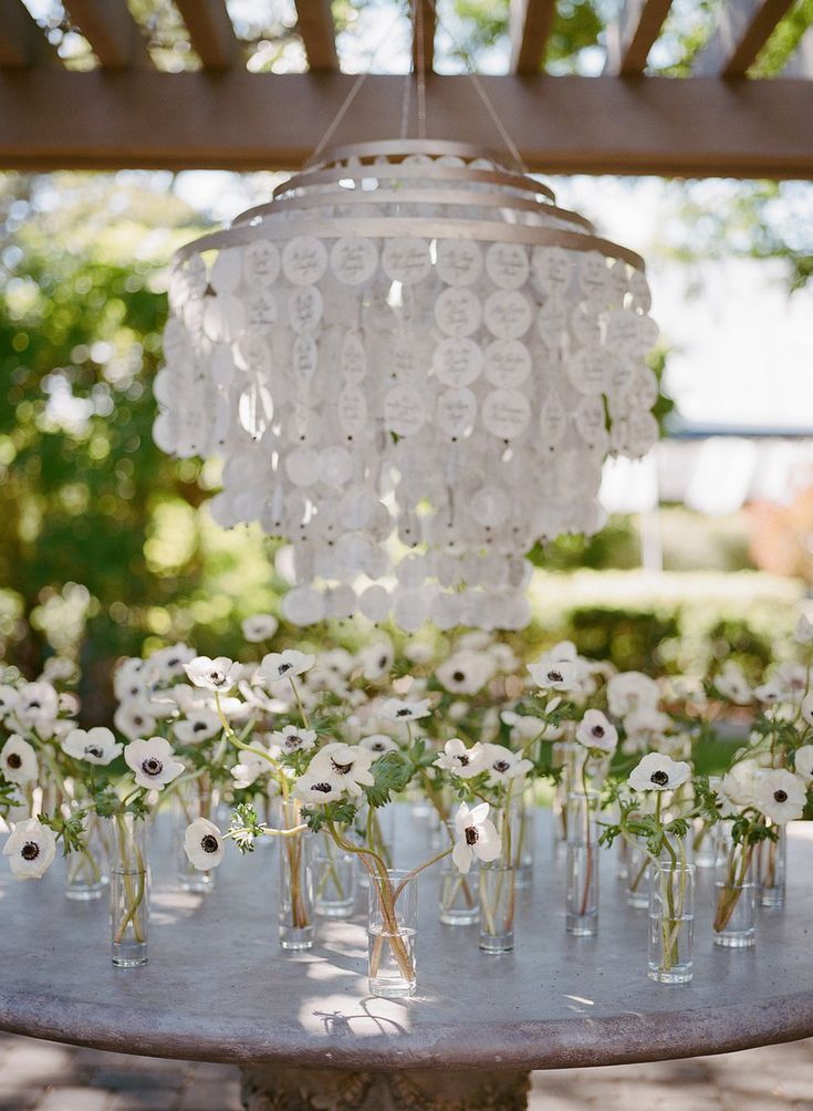 a chandelier filled with white flowers on top of a metal tray under a pergolated roof