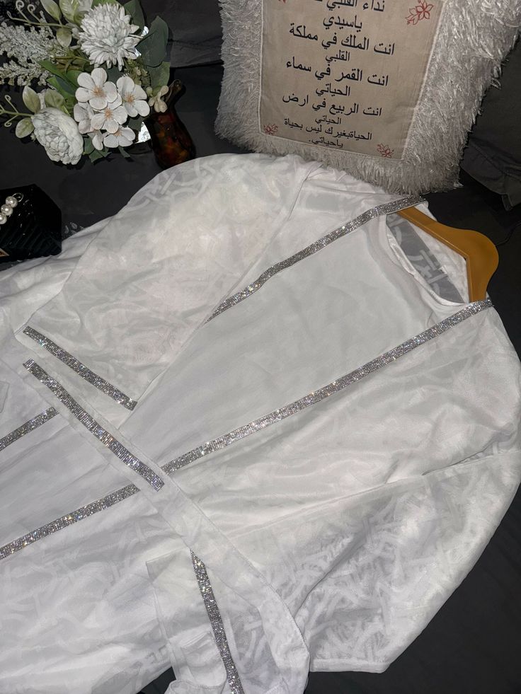 Elevate your style for special occasions with the Noor White Abaya, perfect for nikah ceremonies or parties. Its intricate diamond detailing and elegant design exude sophistication, making it the ideal choice for memorable moments. With a slip dress inner layer, matching hijab, and a dazzling diamond-detailed belt, this abaya ensures you stand out with timeless grace and beauty. Elegant Dabka Gown For Eid, Formal White Dabka Dresses, Elegant Long Thobe For Festive Occasions, Elegant Long Sleeve Thobe With Dabka Embroidery, Elegant Long Sleeve Thobe With Dabka, Elegant Evening Thobe In Maxi Length, Elegant Floor-length Party Thobe, Festive Elegant Maxi Length Thobe, Luxury Wedding Dresses For Eid