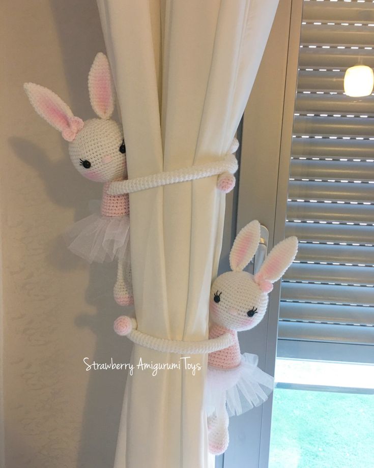 two stuffed animals hanging from the side of a white curtain in front of a window