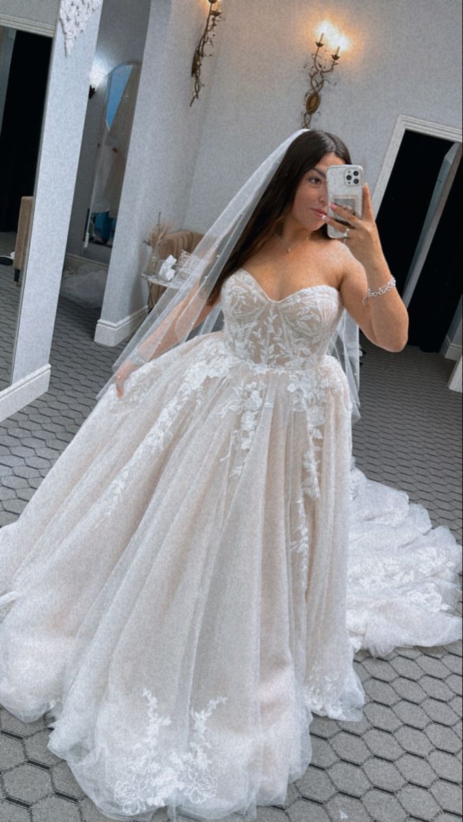 a woman in a wedding dress taking a selfie with her cell phone while wearing a veil