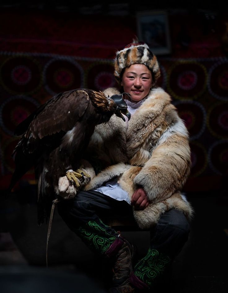 a woman holding a large bird in her hands and wearing an elaborate headdress