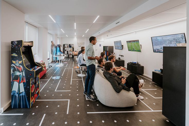 several people are playing video games in an office setting with arcade machines and bowling tables