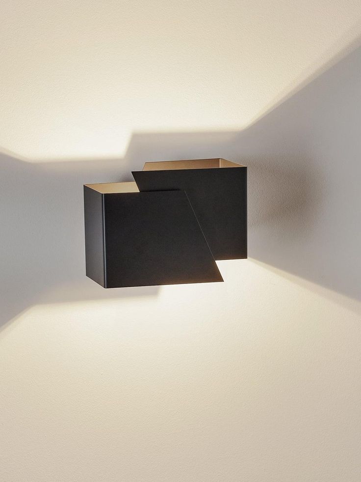 a wall light that is on the side of a white wall with shadows coming from it