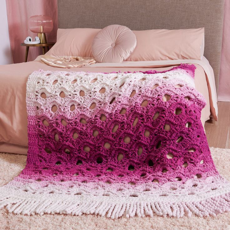 a pink and white crocheted blanket sitting on top of a bed next to pillows