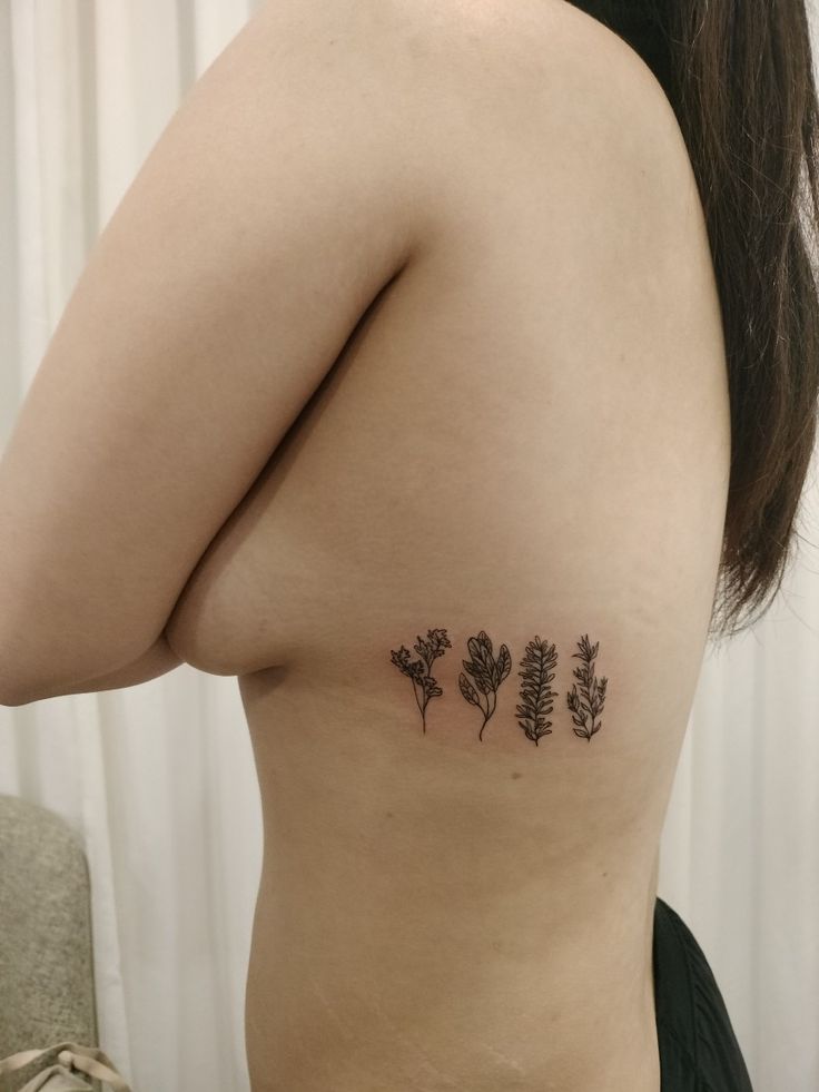 a woman's back with three small flowers on her left side ribcage