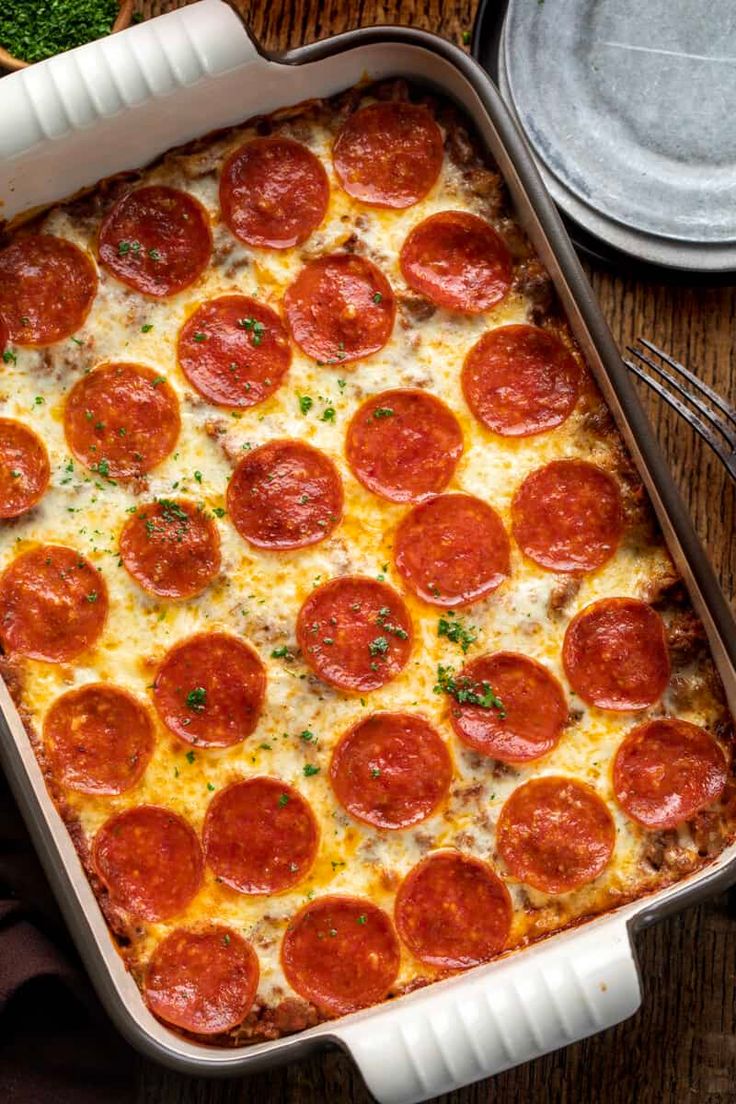 a pizza casserole with pepperoni and cheese in a white dish on a wooden table