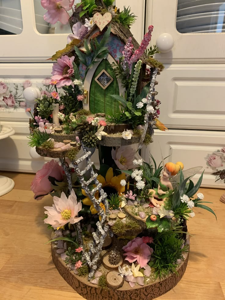 a house made out of flowers and plants on top of a wooden table in front of a white door