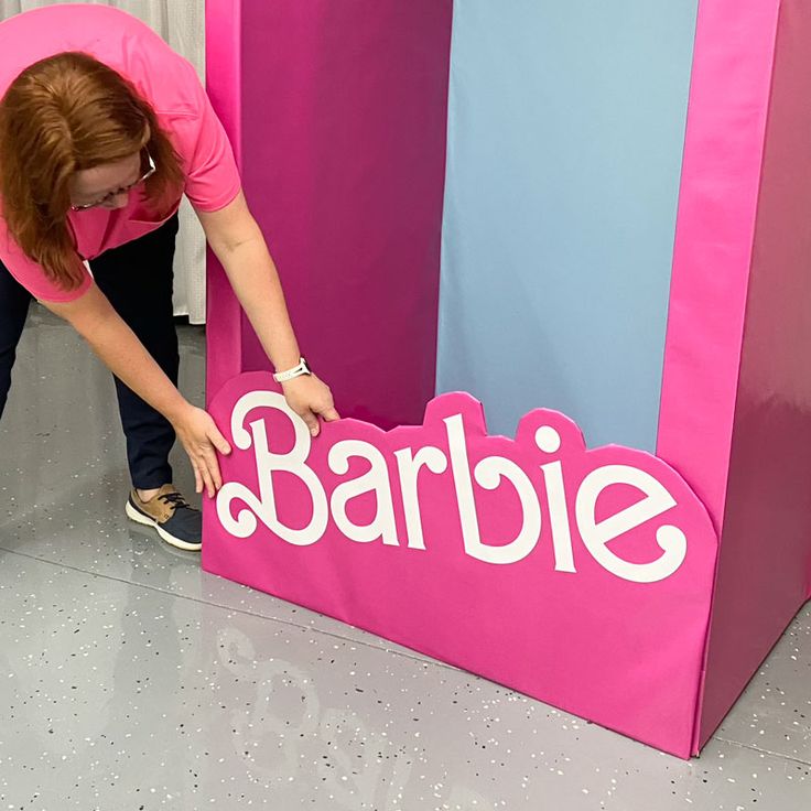 a woman in pink shirt standing next to a barbie sign