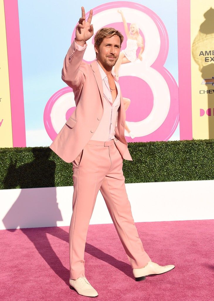 a man in a pink suit waves at the camera while standing on a pink carpet