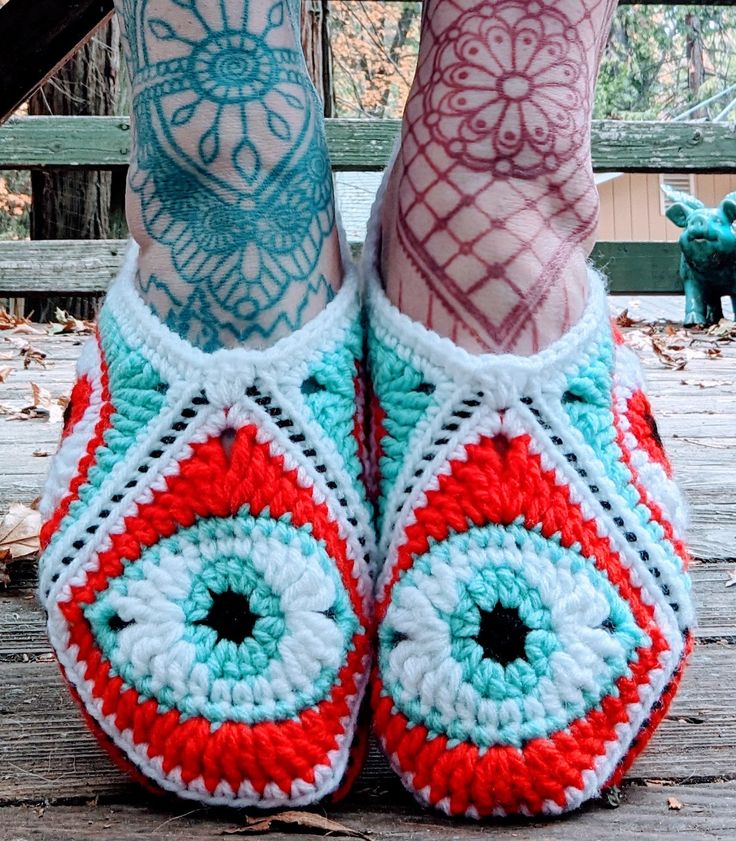 a woman's legs with tattoos and colorful crocheted slippers on them