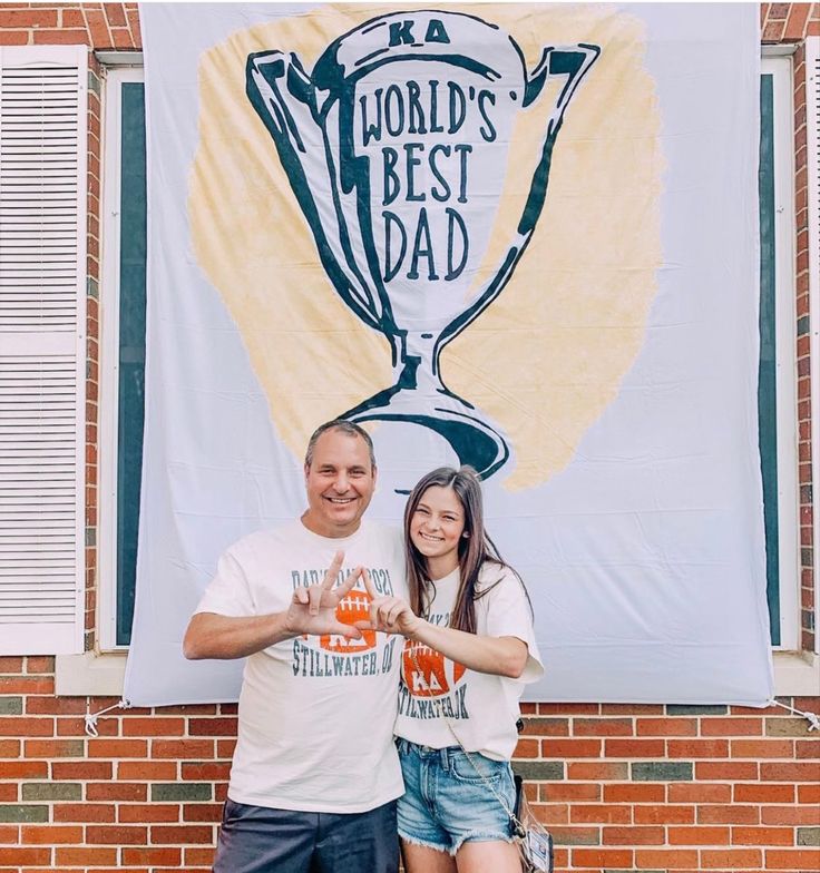 a man and woman standing in front of a sign with the words world's best dad