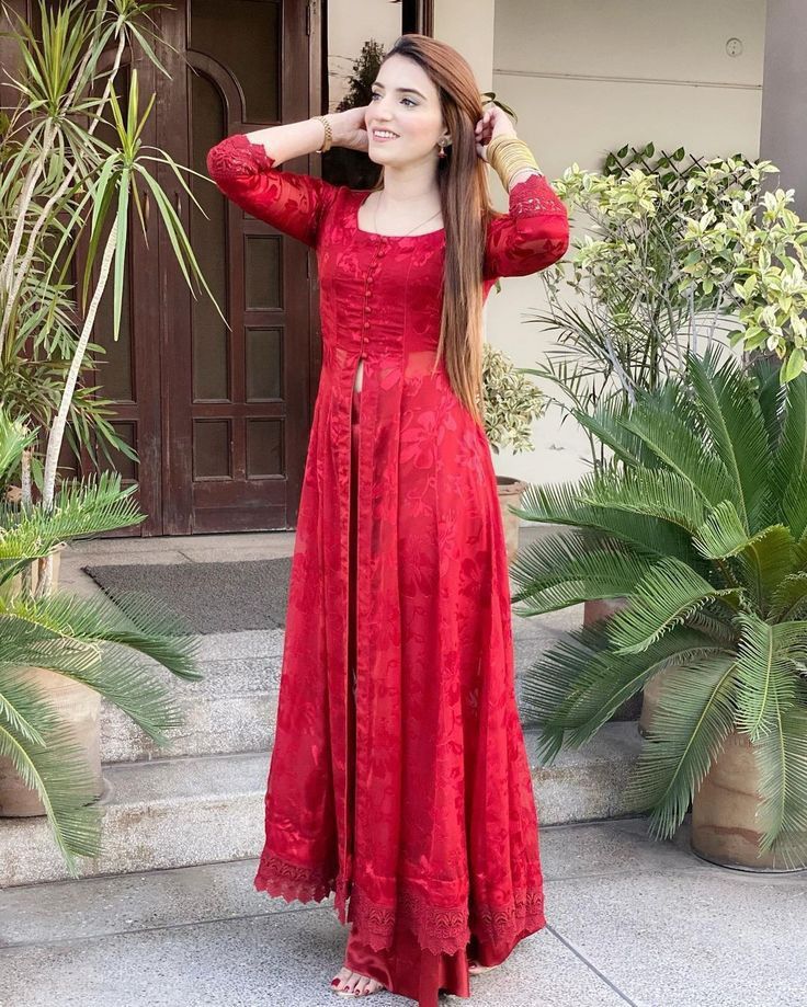 a woman in a red dress standing on steps with her hands behind her head and looking off to the side