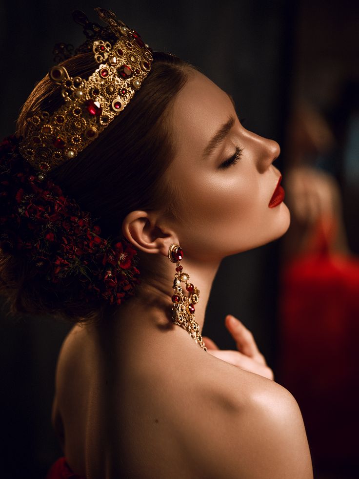 a woman wearing a tiara and red lipstick looks off to the side with her eyes closed