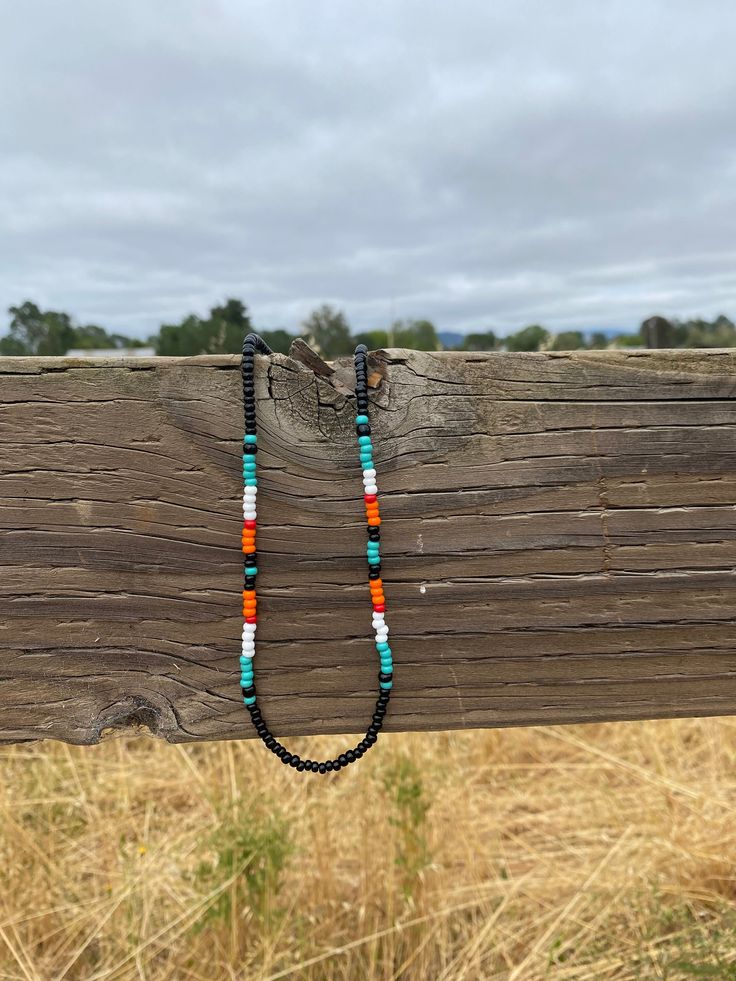 a long beaded necklace is hanging on a wooden fence in front of some dry grass