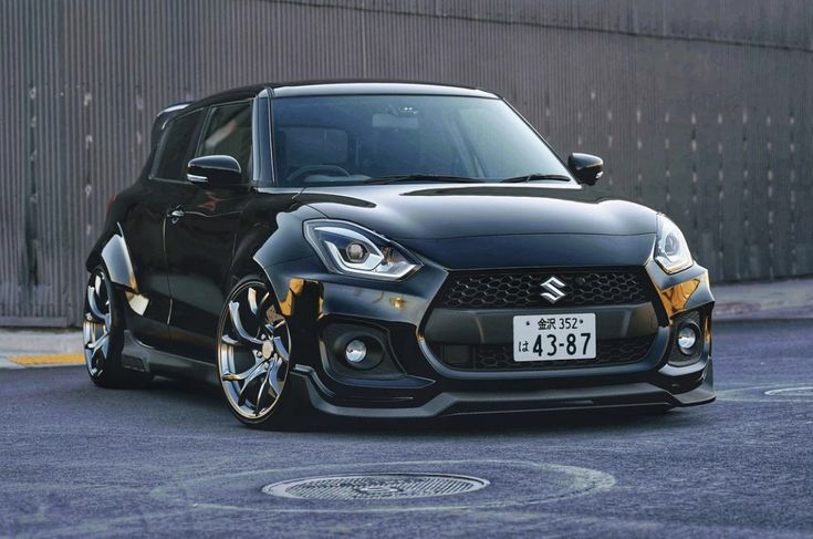 a black suzuki car parked in front of a metal fence with it's door open