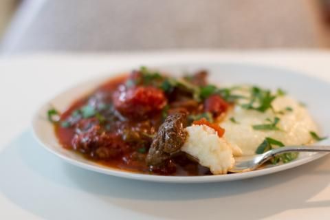 a white plate topped with mashed potatoes covered in meat and gravy next to a fork