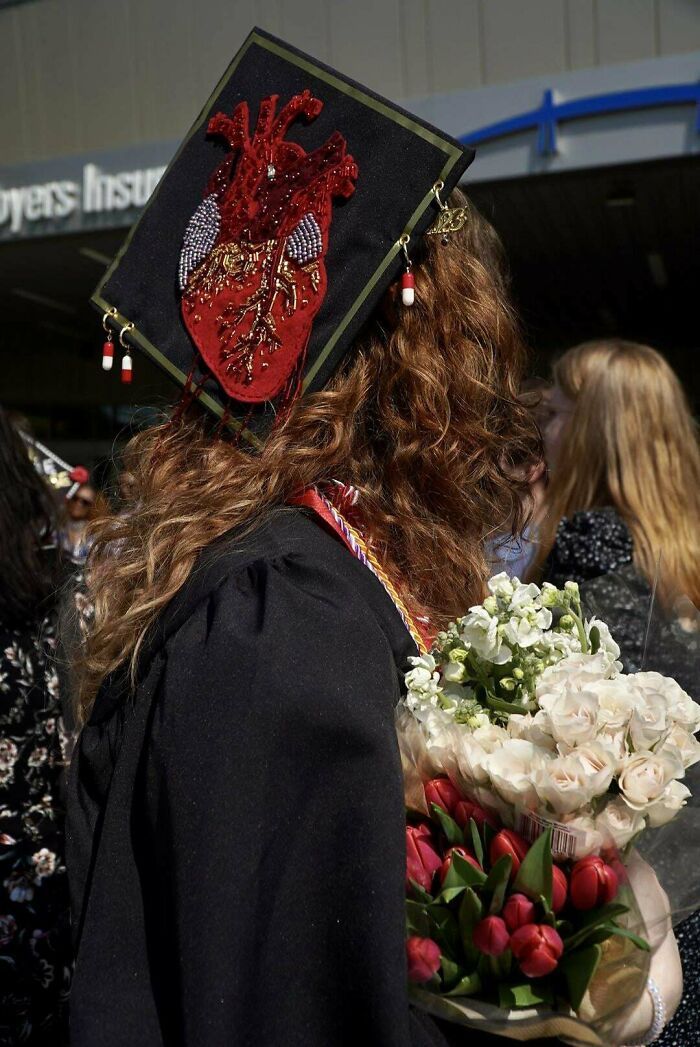 a woman with long hair wearing a graduation cap and holding flowers in her hand while standing outside