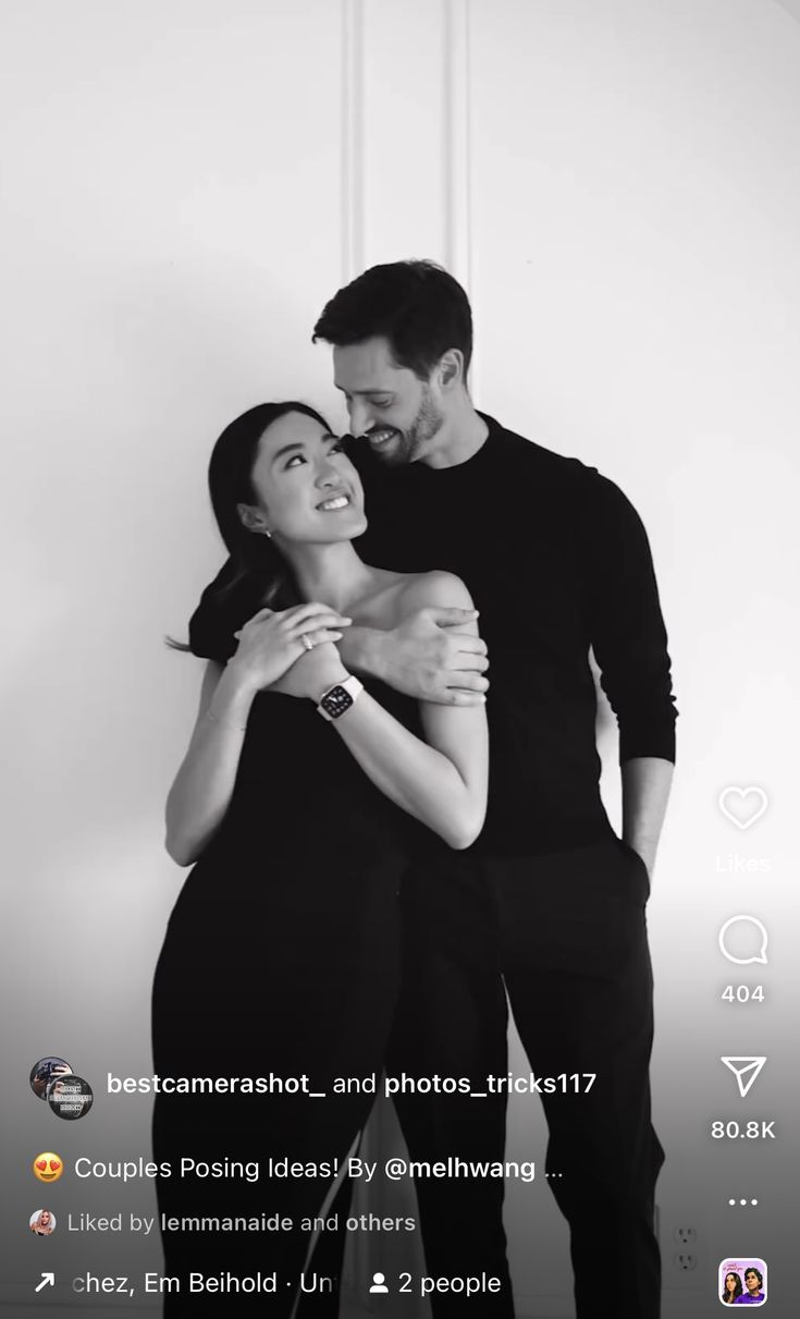 a man and woman hugging each other in front of a white wall with the caption's name on it