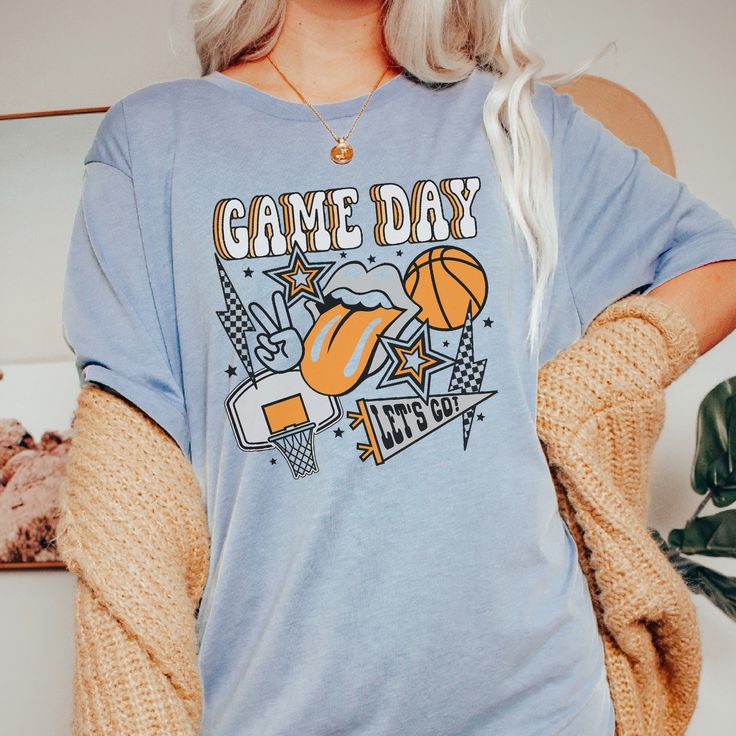 Sport your team spirit in style. Show off your basketball pride with this On The Bleachers Basketball Tee. It's a fun and easy way to show your love for your favorite sport. Go team! Size Guide: we recommend your true size for a loose fit or size down for a fitted fit. Tees are Unisex. Heather blend shirts are 52/48 Cotton/ Poly Blend and Shirts are Unisex. CREW NECK SIZING: Small - Length, 28" Width, 18" (4/6) Medium - Length, 29", Width, 20" (8/10) Large - Length, 30", Width, 22" (12/14) XLarge - Length, 31", Width, 24" (16/18) 2XLarge- Length, 32", Width, 26" (20/22) We recommend comparing these measurements against a shirt that you like the fit of for ordering a tee that will fit best. Crafted Just for You: Our products are made to order, and we're all about delivering that extra touch Casual Basketball T-shirt With Screen Print, Sporty Basketball Team Tops, Team-colored Tops With Team Logo For Basketball, Baseball Season Fan Merchandise Tops With Team Spirit, Sporty Tops For Baseball Season Fan Merchandise, Game Day Sports Season T-shirt With Screen Print, Game Day T-shirt With Screen Print For Sports Season, Team-colored Graphic T-shirt For Game Day, Team-colored Graphic Print T-shirt For Game Day