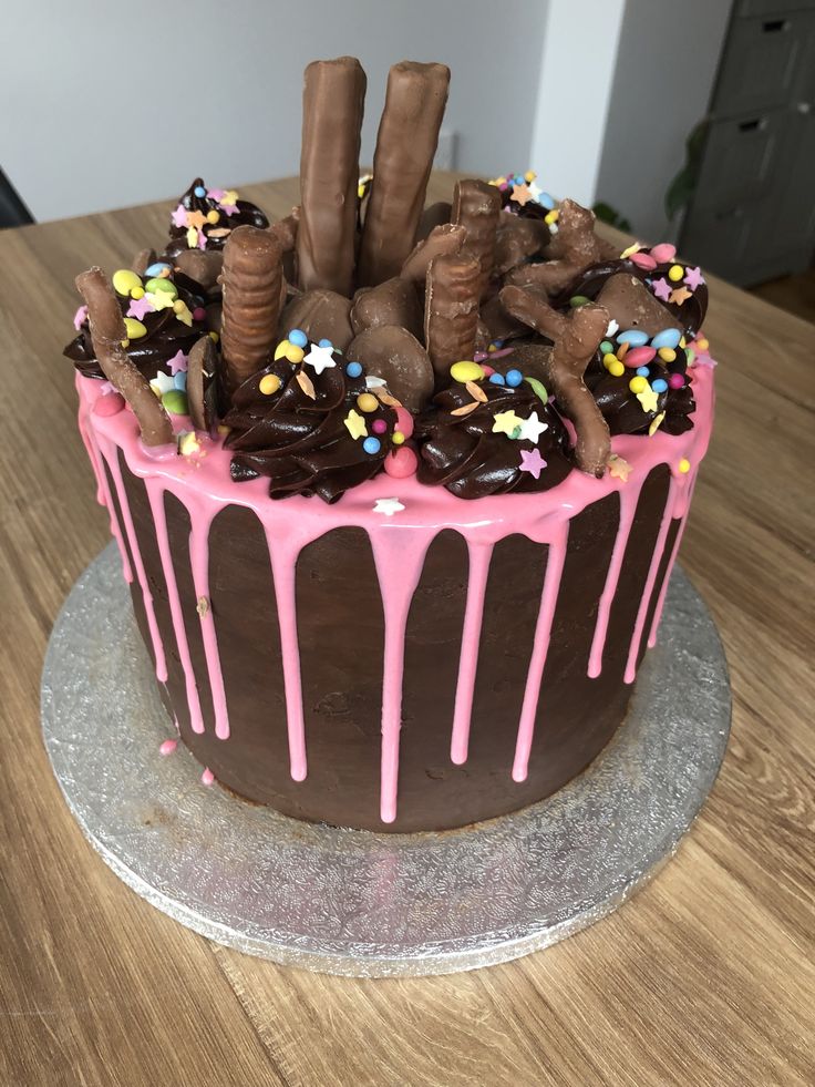 a chocolate cake with pink icing and sprinkles on the top is sitting on a wooden table