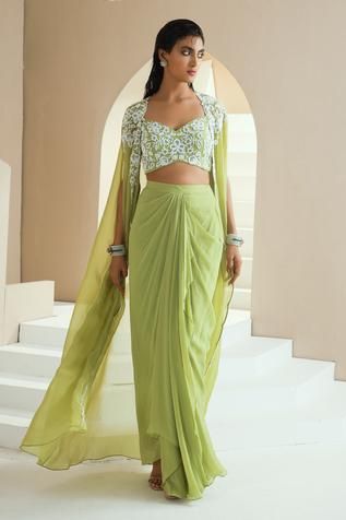 Green long cape with embroidery in pearls, glass beads and white beads. Comes with embroidered choli and draped skirt.
Components:3
Pattern:Embroidered
Type of Work:Floral Motifs
Neckline:Sweetheart
Sleeve Type:Slit Sleeves
Fabric:Skirt and Choli: Georgette, Cape: Organza, Lining: Satin
Color:Green
Other Details:
Floral embroidery
Scalloped hem cape
Draped skirt
Note: The outfit worn by the model on the right is not for sale
Occasion:Mehendi and Haldi - Aza Fashions Lungi Dress Indian For Women, Drape Skirt Outfit Indian, Satin Skirt Outfit Indian, Saree Skirt Drape, Skirt Saree Drape, Long Cape Dress Indian, Drape Skirt Outfit, Bollywood Style Festive Skirt Set With Traditional Drape, Draped Skirt Indian Outfit