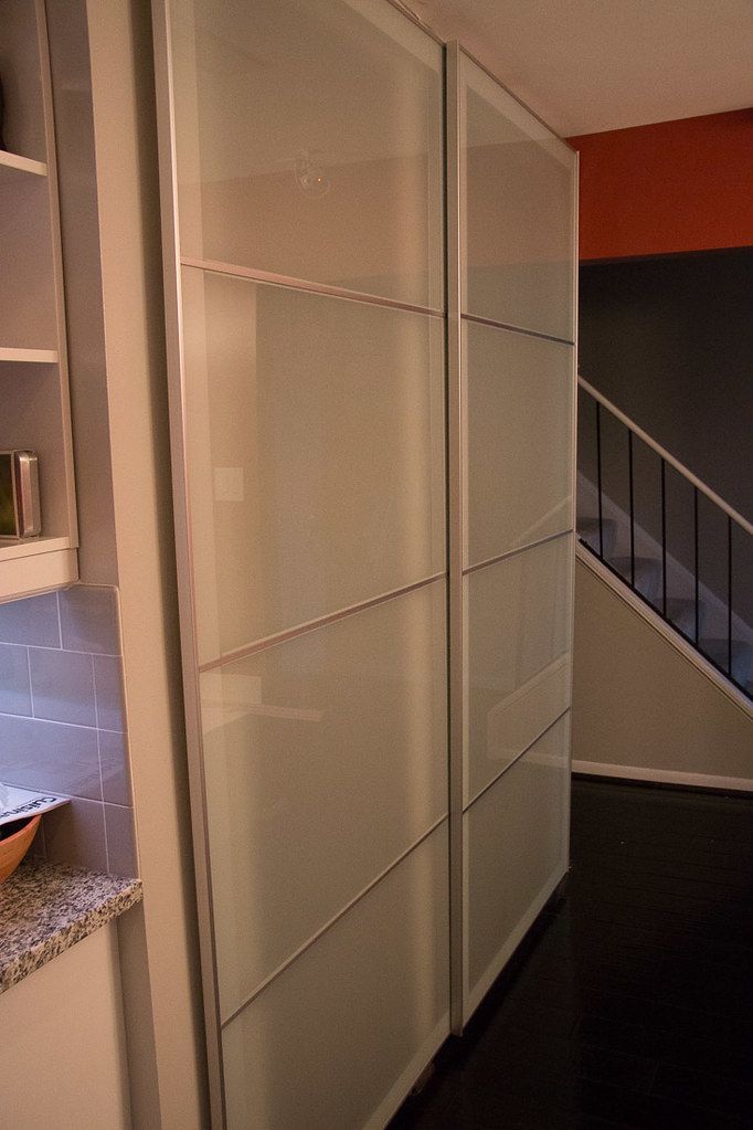 a white closet with glass doors next to a stair case in an orange and black room