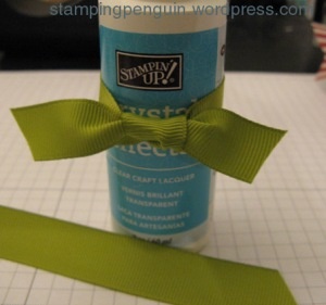 a bottle with a green bow on it sitting next to a piece of ribbon and scissors