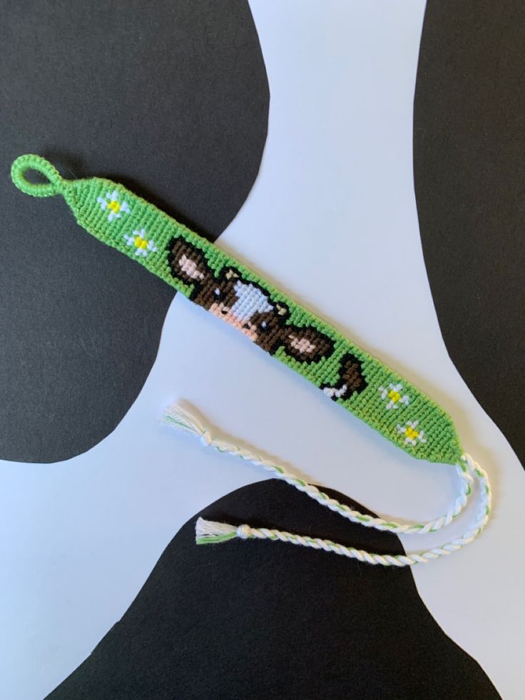 A friendship bracelet with a cow’s face on it on a green background. Cow Friendship Bracelet, Cow Pattern Bracelet, Fnaf Friendship Bracelet, Cow Print Friendship Bracelet Pattern, Cow Bracelet, Cow Friendship Bracelet Pattern, Cow Bracelet Pattern, Chocolate Cow, Winter Bracelet