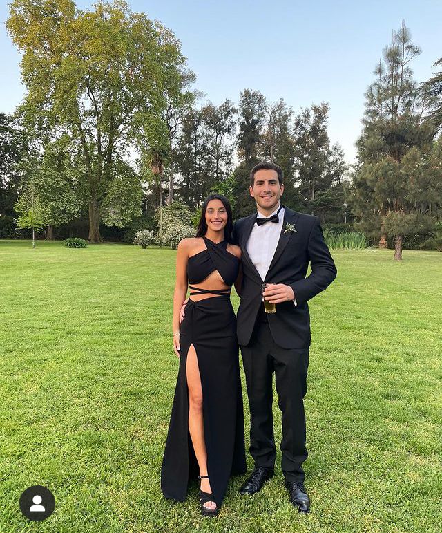 a man and woman in formal wear posing for a photo on the grass with trees in the background