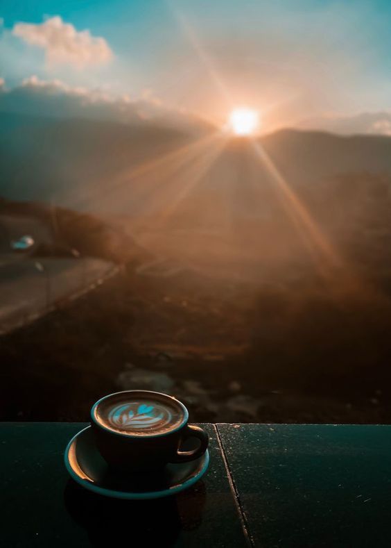 a cup of coffee sitting on top of a wooden table next to a mountain range