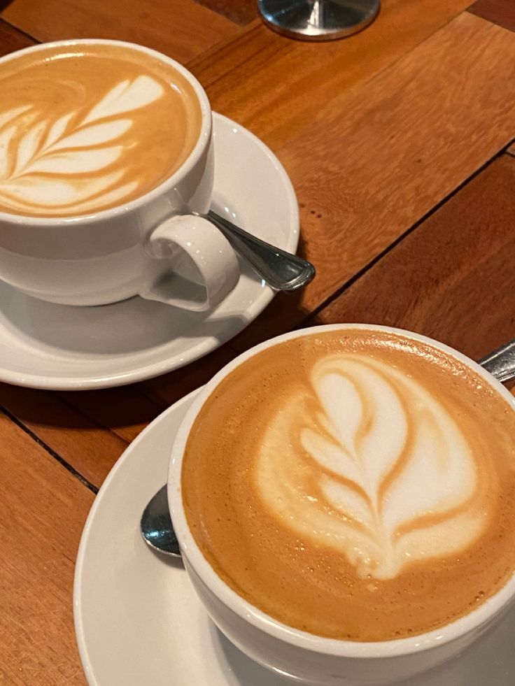 two cups of cappuccino sitting on top of white saucers next to each other